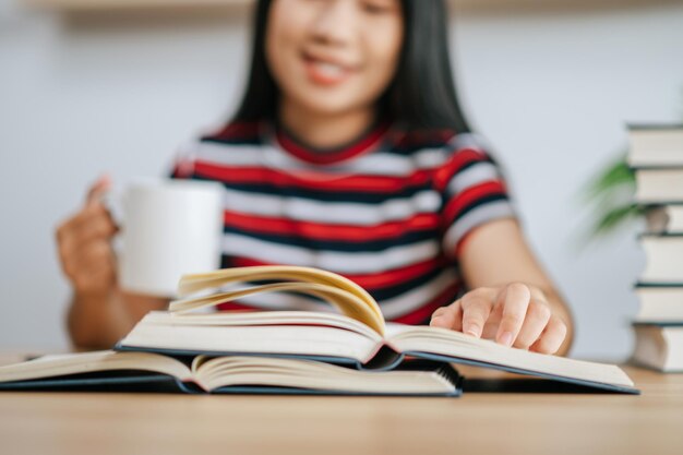 Een jonge vrouw die in een boek op tafel werkt en een koffiekopje vasthoudt