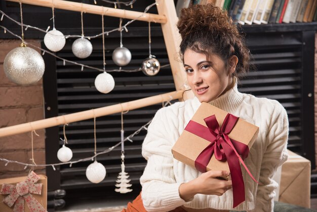 Een jonge vrouw die naar de camera kijkt en een geschenkdoos met strik vasthoudt