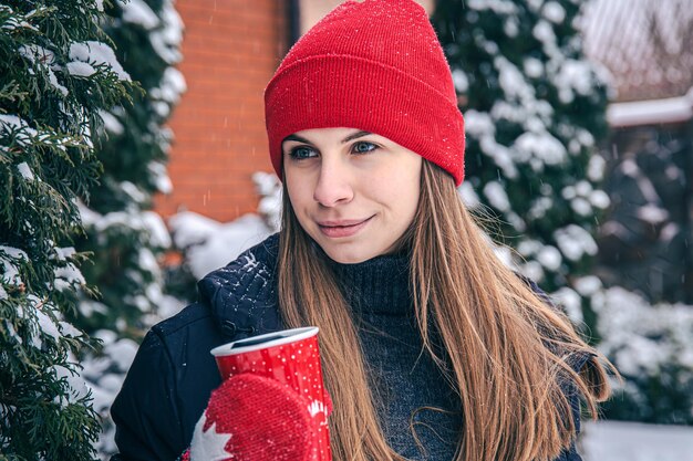 Een jonge vrouw drinkt in de winter een warme drank uit een rode thermische kop