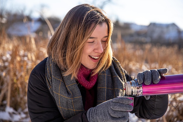 Een jonge vrouw geniet van een warme drank uit een thermoskan tijdens een wandeling in de winter