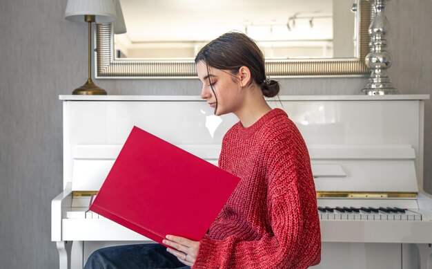Een jonge vrouw in een rode gebreide trui bij een witte piano