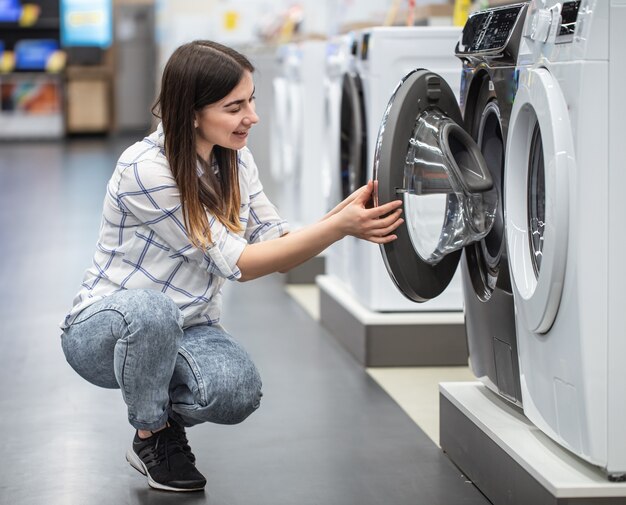 Een jonge vrouw in een winkel kiest een wasmachine .. Het concept van winkelen.