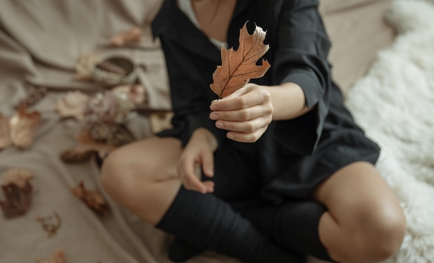 Een jonge vrouw in warme kousen houdt thuis een herfstblad in haar handen.