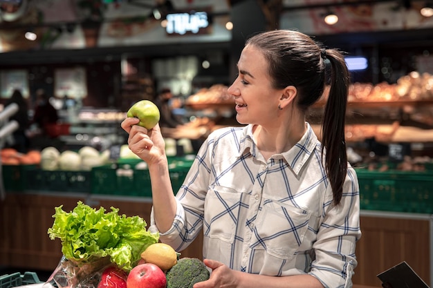 Een jonge vrouw kiest groenten en fruit in een supermarkt