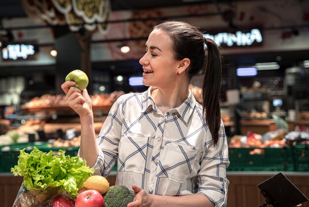 Een jonge vrouw kiest groenten en fruit in een supermarkt