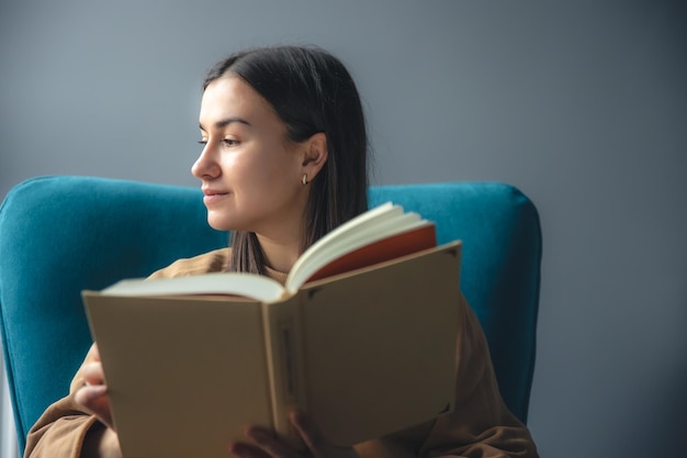 Gratis foto een jonge vrouw leest een boek zittend in een stoel