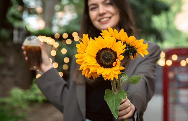 Een jonge vrouw met een boeket zonnebloemen en een koude koffiedrank in de stad