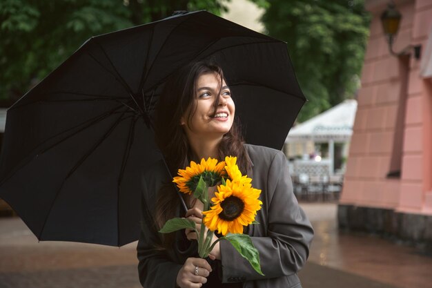 Een jonge vrouw met een boeket zonnebloemen onder een paraplu bij regenachtig weer