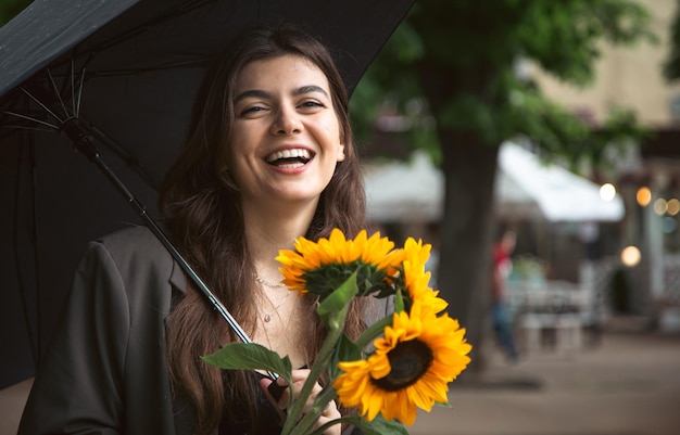 Een jonge vrouw met een boeket zonnebloemen onder een paraplu bij regenachtig weer
