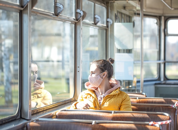 Een jonge vrouw met een masker zit alleen in het openbaar vervoer tijdens de coronaviruspandemie.