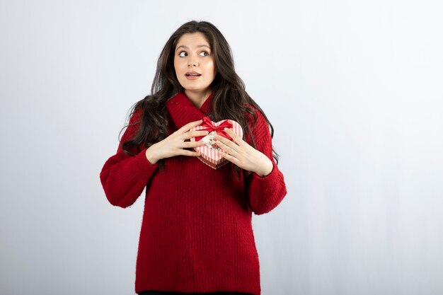 Een jonge vrouw met een rode hartvormige doos geïsoleerd op een witte muur.