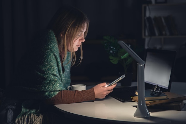 Een jonge vrouw met een smartphone in haar handen werkt 's avonds laat