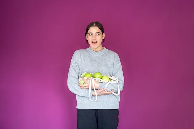 Een jonge vrouw met een stringtas met appels op een roze achtergrond