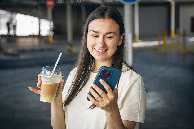 Gratis foto een jonge vrouw met koffie praten aan de telefoon op de parkeerplaats