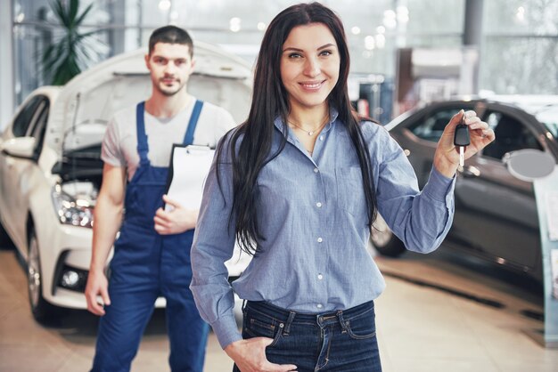 Een jonge vrouw neemt een auto van het autoservicecentrum. Ze is blij omdat het werk perfect is gedaan