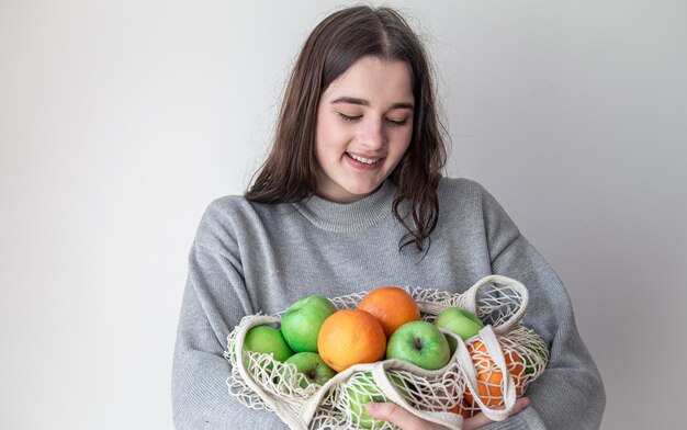 Een jonge vrouw op een witte achtergrond houdt een boodschappentas met vers fruit vast