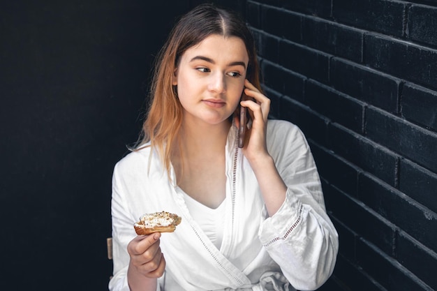 Gratis foto een jonge vrouw praat aan de telefoon en eet een eclair