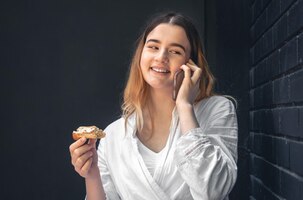 Een jonge vrouw praat aan de telefoon en eet een eclair