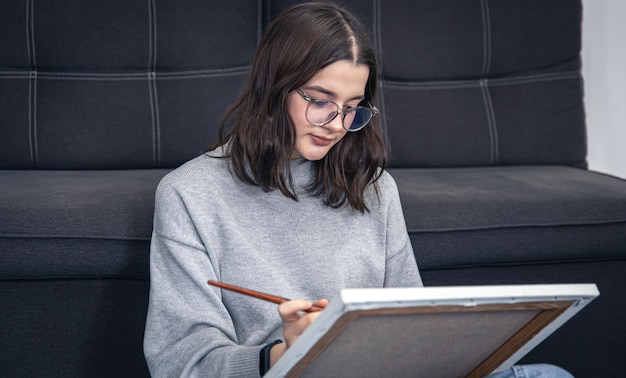 Een jonge vrouw schildert zittend een schilderij op een doek