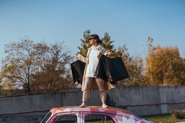 Een jonge vrouw staat in een auto met tassen in haar handen