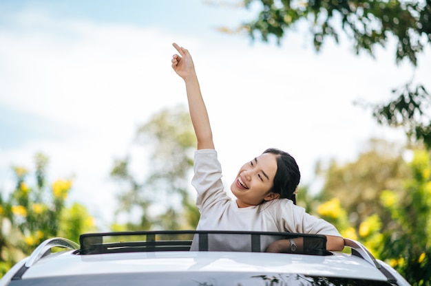 Een jonge vrouw staat vrolijk in de auto vanaf het zonnedak van de auto.