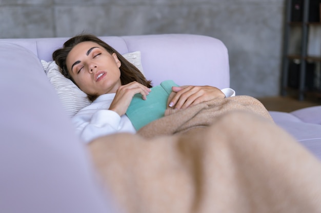 Een jonge vrouw thuis in een witte hoodie op de bank wikkelde zichzelf in een warme deken, viel in slaap en las een boek