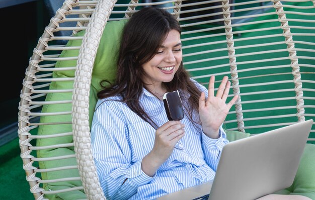 Een jonge vrouw werkt op een laptop en eet een ijsje in een hangmat