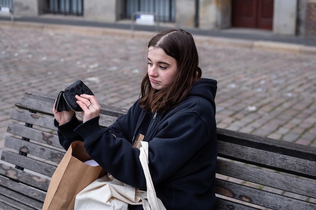 Een jonge vrouw zit op een bank met een leeg portefeuilleconcept gebrek aan geld