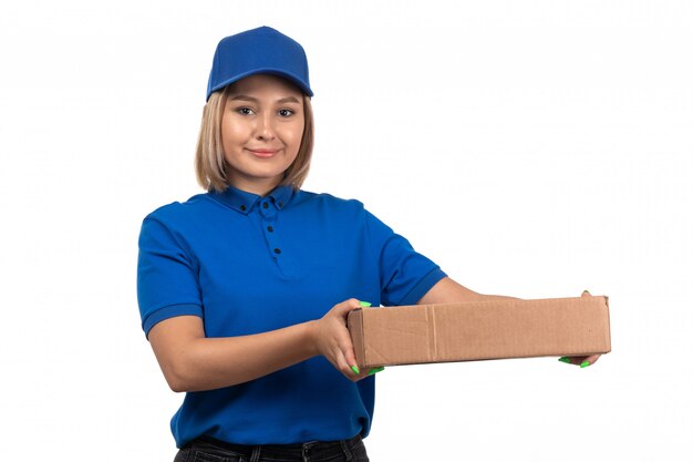 Een jonge vrouwelijke koerier vooraanzicht in blauw uniform de leveringspakket van het holdingsvoedsel met glimlach op haar gezicht