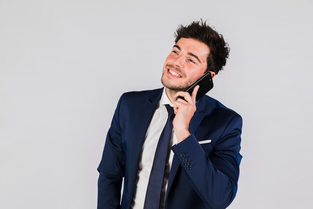 Een jonge zakenman die op mobiele telefoon tegen grijze achtergrond spreekt