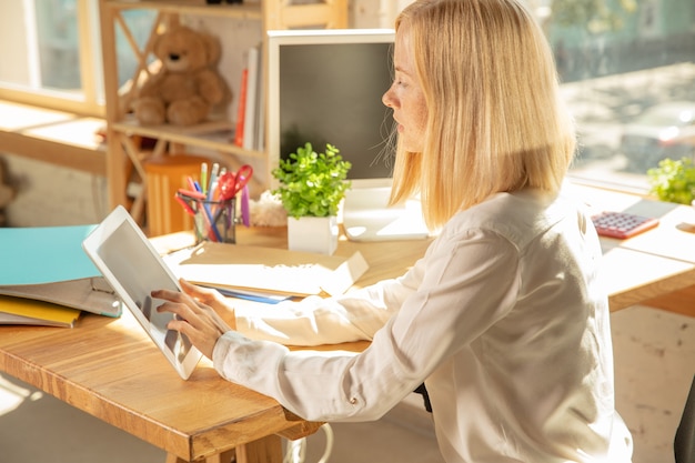 Een jonge zakenvrouw die zich op kantoor beweegt en een nieuwe werkplek krijgt. Jonge blanke vrouwelijke beambte rust nieuwe kast uit na promotie. Met behulp van tablet. Business, lifestyle, nieuw levensconcept.