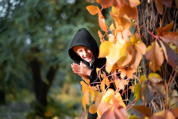 Een jongen in zwarte kleren staat bij een boom waaraan gele herfstbladeren hangen