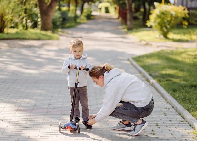 Een jongen met zijn moeder rijden in het park op een scooter