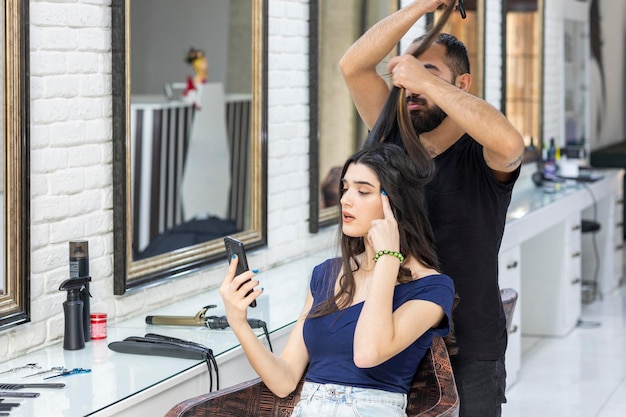 Een kapper die het haar van een meisje van 39 uitrekt en een meisje dat naar haar telefoon kijkt Foto van hoge kwaliteit