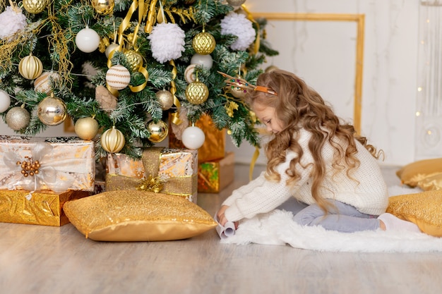 Een kind legt thuis een brief voor de kerstman onder een kerstboom met een gouden decor Premium Foto
