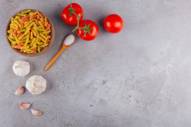 Een kleikom van multi gekleurde ruwe spiraalvormige deegwaren met knoflook en verse rode tomaten.