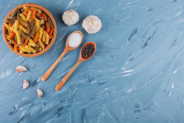 Een kleikom van veelkleurige rauwe spiraalvormige pasta met knoflook en kruiden.