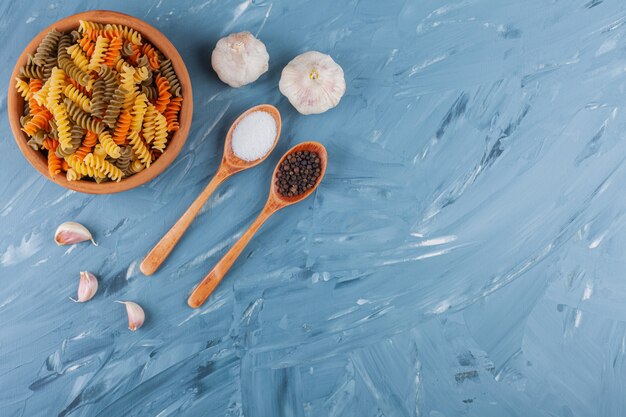 Een kleikom van veelkleurige rauwe spiraalvormige pasta met knoflook en kruiden.