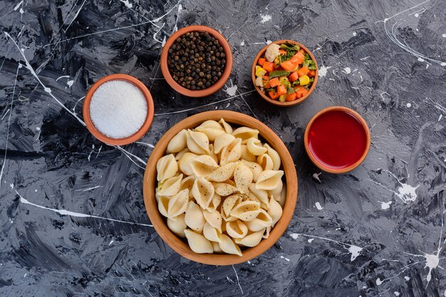 Een kleikom vol schelppasta met tomatensaus op een marmeren ondergrond