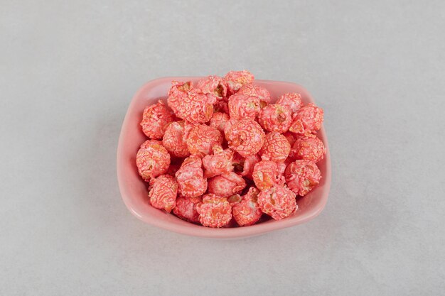 Een klein hoopje gearomatiseerde popcorn op een roze schaal op marmeren tafel.