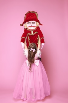 Een klein meisje als schoonheid ballerina op roze lange jurk met notenkraker op roze studio