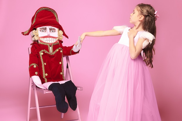 Een klein meisje als schoonheid ballerina op roze lange jurk met notenkraker op roze studio