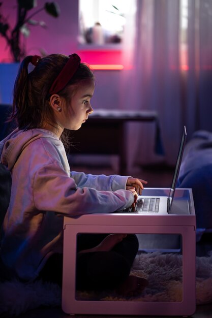 Een klein meisje gebruikt een laptop terwijl ze in een kamer met neonverlichting zit