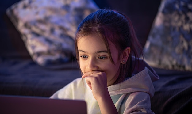 Een klein meisje gebruikt 's avonds laat een laptop Premium Foto