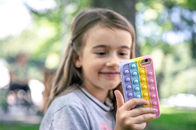 Een klein meisje houdt in haar hand een telefoon in een hoesje met puistjes erop, een trendy anti-stress speeltje.