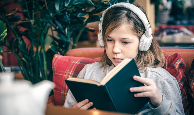 Een klein meisje leest een boek en luistert naar muziek op een koptelefoon