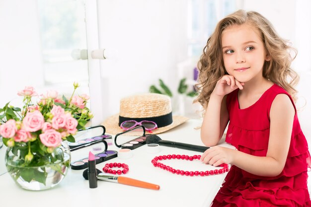 Een klein meisje met cosmetica. Ze zit in de slaapkamer van moeder, bij de spiegel.