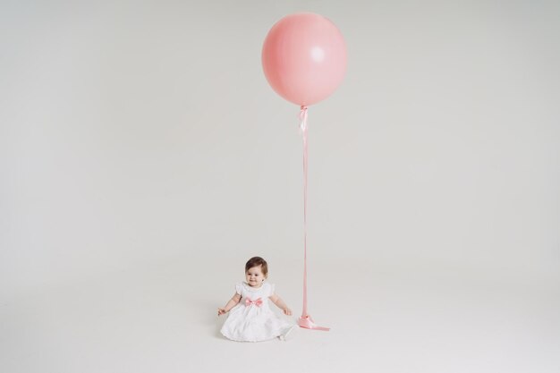 Een klein meisje met een grote roze ballon in een witte jurk op een witte achtergrond