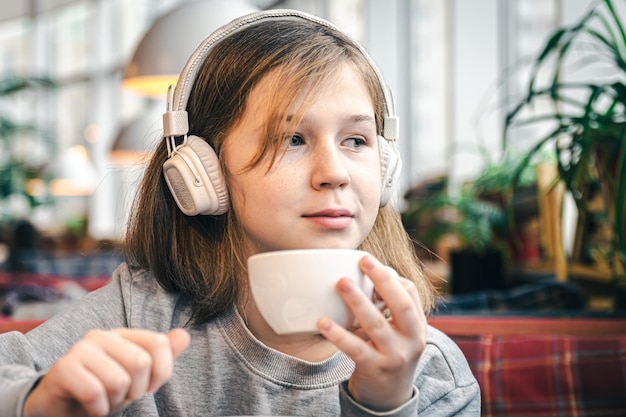 Een klein meisje met een koptelefoon in een café met een kopje thee