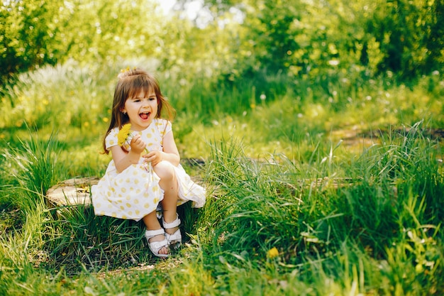 een klein meisje met prachtig lang haar en in een gele jurk speelt in het zomerpark